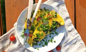 Pyszny omlet ze szpinakiem i pomidorkami, posypany szczypiorkiem, czeka na talerzu. Idealny na letnie śniadanie.