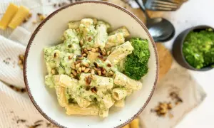 Eine Schüssel Rigatoni mit cremiger **Brokkoli Sahne Sauce** und Pinienkernen garniert. Daneben ein kleiner Napf mit gehacktem Brokkoli und Käse.