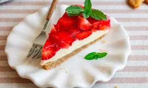 Ein Stück Kuchen ohne Backen mit Keksboden, belegt mit frischen Erdbeeren und Sahne, garniert mit Minze.