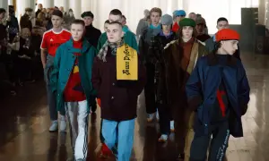 Młodzi mężczyźni prezentują nowoczesny turecki ubiór męski na wybiegu. Wśród nich wyróżnia się żółty szalik z napisem "Доша Рубчински Россия".