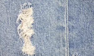 Zbliżenie na niebieski denim z widocznym przetarciem. Dowiedz się, jak zrobic przetarcia na dzinsach, by nadać im stylowy, znoszony wygląd.