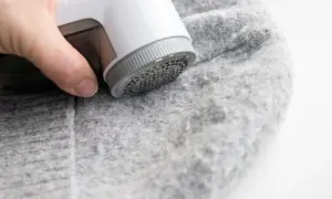 Ein Wollpullover, der eingelaufen ist, wird mit einem Fusselrasierer von Knötchen befreit.