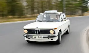 Vit BMW 70-talsklassiker kör på en väg, med en man bakom ratten.