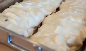 Dwa surowe strudle z jabłkami w metalowej formie, gotowe do pieczenia. Ciasto jest błyszczące i lekko złociste.