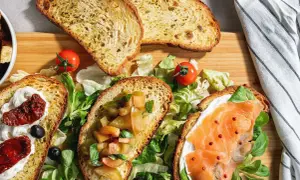 Bruschette senza pomodoro: fette di pane tostato con salmone, crema, pomodori secchi e verdure fresche.