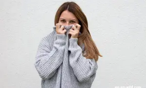 Frau versteckt sich hinter ihrem kuscheligen Pullover, der sich statisch aufgeladen anfühlt.