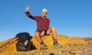 Glücklicher Wanderer mit Rucksack und Stöcken auf einer felsigen Anhöhe, genießt die Aussicht nach einer Etappe des Fischerpfads in Portugal.