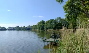 Wędkarz na pomoście nad spokojnym zalewem w Nowym Mieście. Otoczenie zieleni i błękitne niebo tworzą sielski krajobraz.