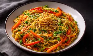 Schüssel mit chinesischen Bratnudeln, garniert mit Erbsen, Paprika und Sesam.
