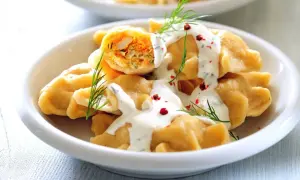 Pierogi z farszem warzywnym polane sosem, udekorowane koperkiem i pieprzem.