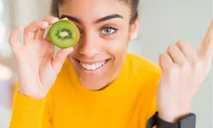 Junge Frau hält Kiwi vor ihr Auge, ein Symbol für gesunde Ernährung und eine gesunde Leber.
