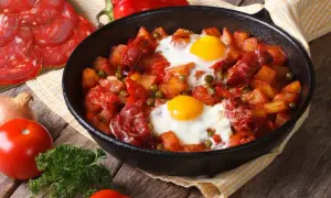 Pyszny obiad z jajek, ziemniaków, chorizo i groszku w patelni. Obok pomidory, cebula i natka pietruszki.
