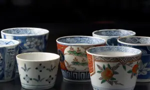 Vielfalt der japanischen Porzellankunst: Mehrere kleine Becher mit traditionellen Mustern, darunter Blumen und geometrische Formen, auf dunklem Hintergrund.