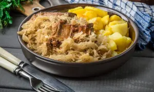 Pyszne żeberka w kapuście z ziemniakami, podane w misie. Obok sztućce i serwetka.