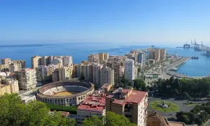 Vista panorámica desde el mirador de Gibralfaro: la plaza de toros, el puerto y la ciudad de Málaga bajo un cielo azul.