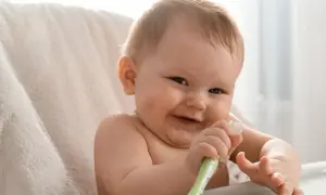 Uśmiechnięte dziecko bawi się swoją pierwszą szczoteczką do zębów.