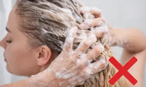 Mani che massaggiano shampoo sui capelli biondi, con una croce rossa che indica di evitare certi rimedi capelli grassi.