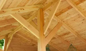 Drewniana konstrukcja dachu szopy, budowa szopy drewnianej bez pozwolenia. Widoczne belki i deski, wiszące klatki dla ptaków.