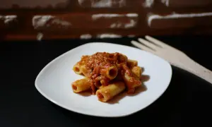 Piatto di pasta alla portofino con sugo rosso e forchetta in legno sullo sfondo di mattoni.