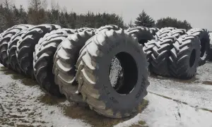 Duże opony rolnicze, pokryte śniegiem, czekają na utylizację. W tle las i zimowy krajobraz.
