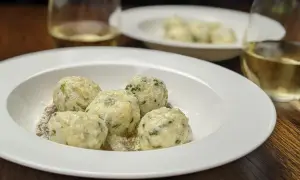 En tallrik med fluffiga gnudi, perfekt för ett enkelt gnudi recept. Serveras med riven ost och ett glas vitt vin.