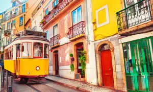Żółty tramwaj przemierza ulicę w Lizbonie w marcu, mijając kolorowe kamienice z azulejos i ozdobnymi balkonami.