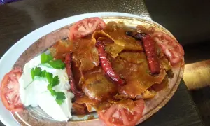 Iskender kebab z sosem pomidorowym, jogurtem, papryczkami i pomidorami.