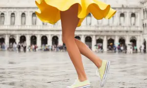 Nogi w żółtej sukience i stylowe buty sportowe do sukienki na mokrym placu w Wenecji.