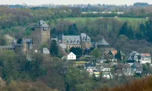 Zamek Schloss Burg w Solingen, otoczony zielenią, z wieżami i budynkami mieszkalnymi u podnóża.