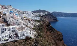 Białe domy Santorini na klifie, z błękitnymi kopułami kościołów, nad lazurowym morzem. Krajobraz jak po trzęsieniu ziemi, ale pełen życia.