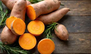 Pomarańczowe bataty, niektóre przekrojone, leżą na drewnianym blacie z gałązkami rozmarynu. Czy pies może jeść bataty? Tak, to zdrowy przysmak!