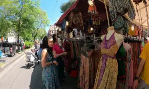 Persone curiosano tra le bancarelle colorate della fiera di San Ciriaco, ammirando abiti etnici e tessuti vivaci sotto il sole.