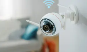 Caméra de surveillance Wi-Fi blanche fixée au mur, avec un symbole Wi-Fi bleu au-dessus. Vous vous demandez pourquoi ma caméra ne se connecte pas en wifi ?