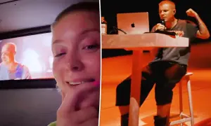 A woman watches a screen showing Justin Parker performing, with a laptop and microphone on a table.