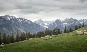 Wędrowiec na zielonym stoku w Beskidzie Niskim, w tle skaliste szczyty z resztkami śniegu.