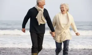 Szczęśliwa para seniorów biegnie plażą, trzymając się za ręce. Idealne tanie wycieczki dla seniorów, by cieszyć się wspólnym czasem.