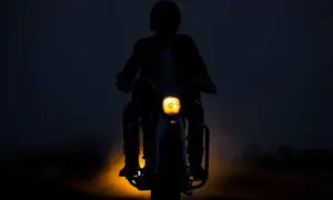 Silhouette d'une personne conduisant une moto dans l'obscurité, le phare jaune illuminant la route. L'aventure de conduire la nuit.