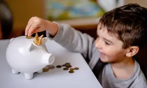 Chłopiec wkłada monetę do skarbonki w kształcie świnki z koroną.