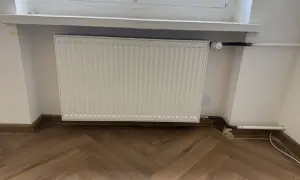 Biały grzejnik pod oknem, nowe podłączenie. Zastanawiasz się, ile kosztuje wymiana kaloryfera?