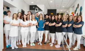 Zespół stomatologów w białych i granatowych uniformach stoi w gabinecie.