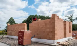 Budowa domu z pustaków ceramicznych Porotherm. Murarz układa kolejne warstwy cegieł.