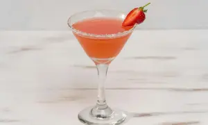 En rosa strawberry daiquiri i ett martiniglas med socker på kanten och en jordgubbsklyfta som garnering.