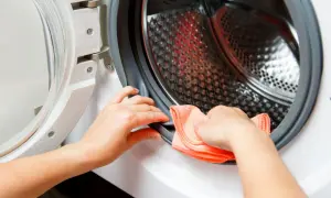 Ręce czyszczą uszczelkę pralki pomarańczową ściereczką. Dowiedz się, jak wyczyścić pralkę, aby służyła dłużej.