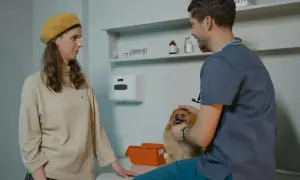 Kobieta z psem u weterynarza. Lekarz bada małego, puszystego pieska, a właścicielka obserwuje.