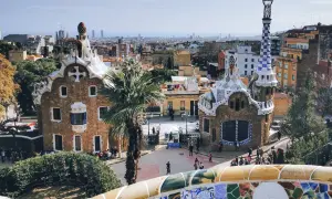 Bunte Mosaike und märchenhafte Gebäude im Park Güell, ein Wahrzeichen von Barcelona. Die Skyline der Stadt im Hintergrund.