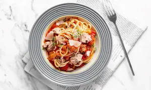 Pyszny makaron z tuńczykiem w sosie pomidorowym, posypany parmezanem i ziołami, podany na talerzu na tle gazety.