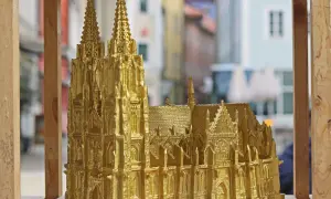 Goldene Nachbildung des Regensburger Doms mit filigranen Figuren und Türmen, die vor einer unscharfen Stadtkulisse steht.