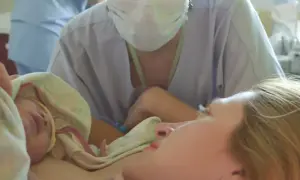 Noworodek przytulony do mamy, personel medyczny w tle. To piękny poród lotosowy, pełen miłości i spokoju.