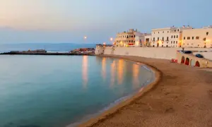 La costa di un paese vicino a Lecce al tramonto, con edifici bianchi, una spiaggia sabbiosa e il mare calmo.