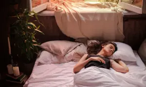 A woman sleeps alone in a rumpled bed, a scene that could represent the quiet solitude of sleep divorce.